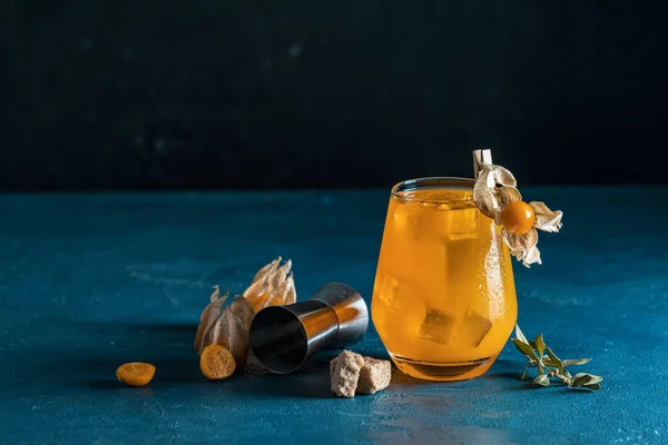 Cocktail laranja amarelo com tangerina e alecrim em vidro com gotas de água decorado Physalis peruviana e açúcar mascavo em fundo escuro com bokeh. Natal e Ano Novo bebida de boas-vindas . — Fotografia de Stock