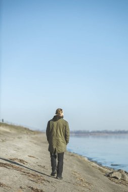 Güneşli bir sabahta sisli bir nehrin kenarında ceketli, sakallı bir adamın dikiz görüntüsü..