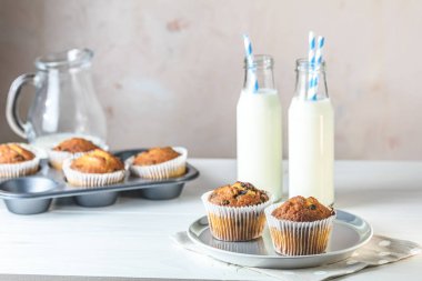 Kağıt bardaklarda vanilyalı karamelli kekler ve beyaz ahşap arka planda bir şişe süt. Lezzetli kek. Ev yapımı bisküvi kekleri. Metin için alanı kopyala.