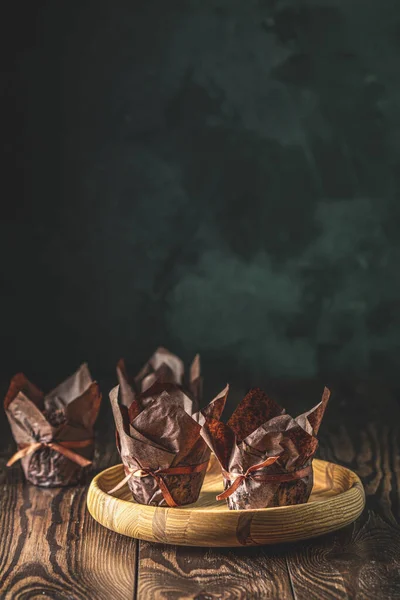 Шоколадные кексы в коричневой бумаге с лентой на деревянной миске. Закрыть, низкая глубина поля, приветственный состав еды . — стоковое фото
