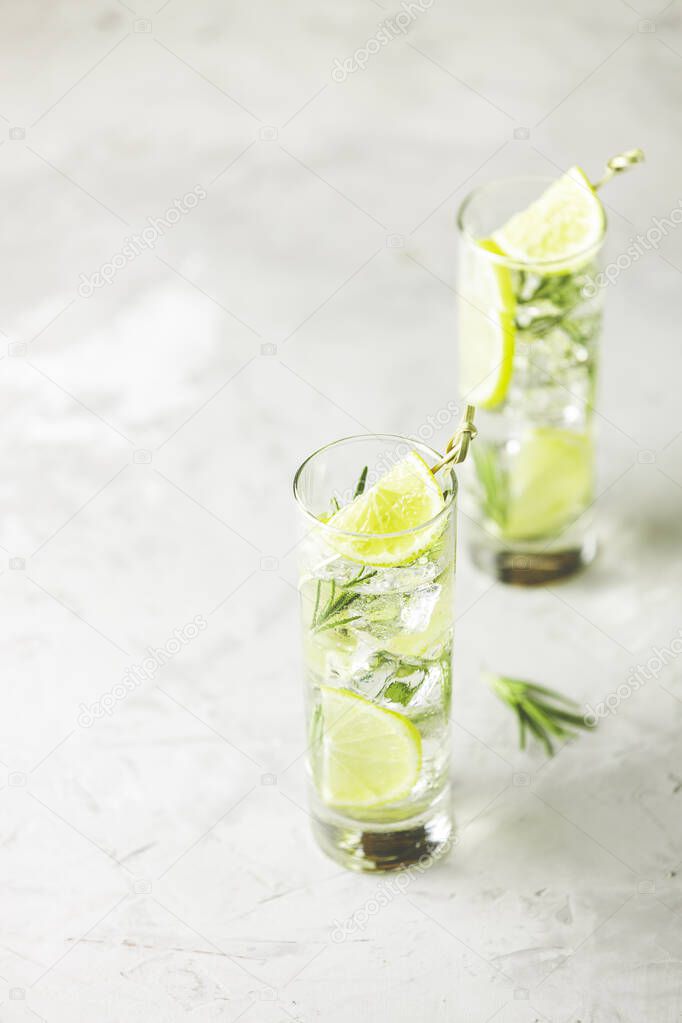 Refreshing lemon lime drink with ice cubes in glass goblets against a light gray background. Summer fresh lemon soda cocktail with rosemary, selective focus.