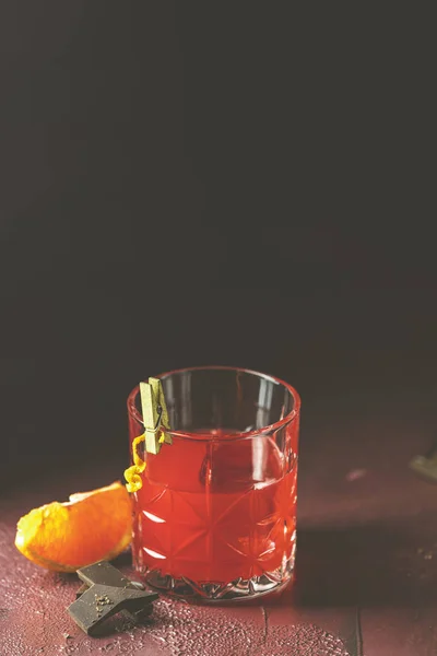 Copa de chocolate negroni naranja roja, un cóctel italiano, un aperitivo, mezclado por primera vez en Firenze, Italia, en 1919, cóctel amargo alcohólico servido con ingredientes en la mesa de burdeos claret oscuro — Foto de Stock