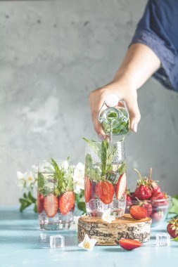 Kadın eli cam şişeden bardağa çilek, buz ve nane ile detoks suyu döküyor. Yaz taze naneli soda kokteyli, seçici odaklanma..