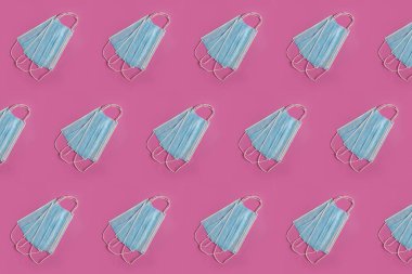 Pembe arka planda, virüs ve bakterilerden korunmak için ağız ve burnu kaplayan birçok mavi tıbbi maske var. Salgın hastalık konsepti. Düzenli kalıp, düz yatış.
