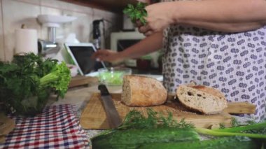 Kadın salataya taze dereotu ekliyor ve mutfakta tablet kullanıyor. Balzamik sirke, yağ ve biber, tuz, baharat, otlar, ahşap tahta, cam kase. Odaklanmayı ayarla. 