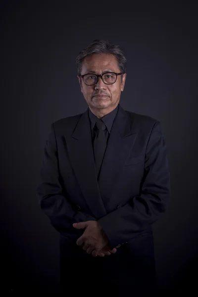 Porträtt av 60-talet asiatiska man bär svart kostym, fotografering i svagt ljus — Stockfoto