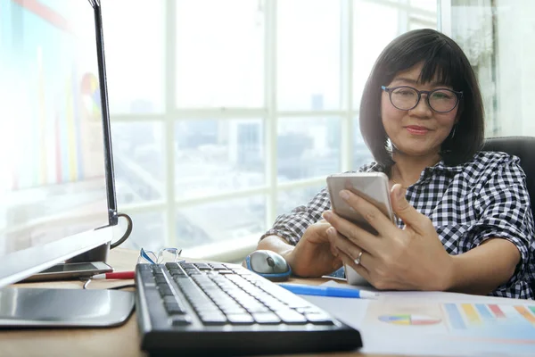 Asijské pracující žena hledá do chytrého telefonu a usmívá štěstí — Stock fotografie