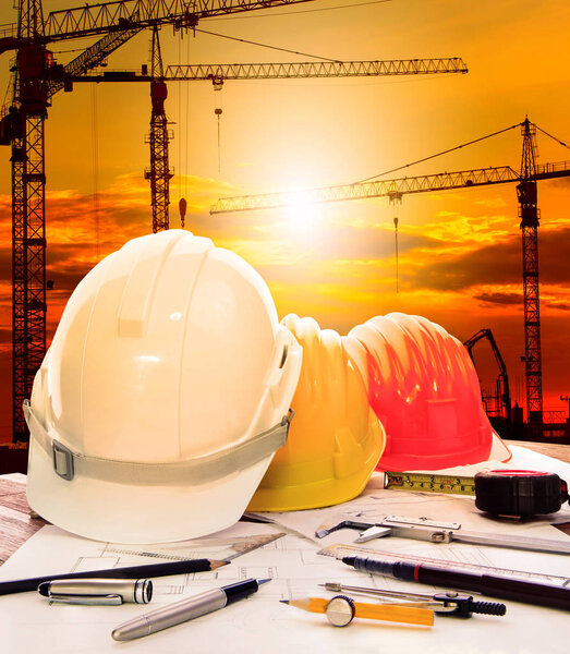 safety helmet on engineer working table and crane construction site background