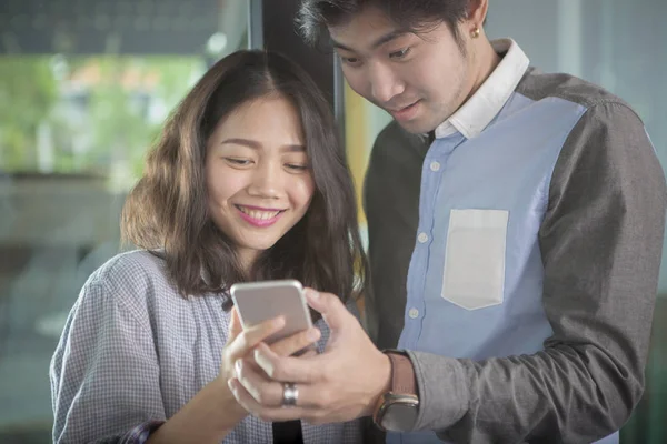 Ásia mais jovem homem e mulher olhando para inteligente telefone tela toothy — Fotografia de Stock