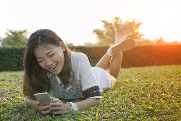 Asian younger woman lying on field playing smart phone and laugh — Stock Photo, Image