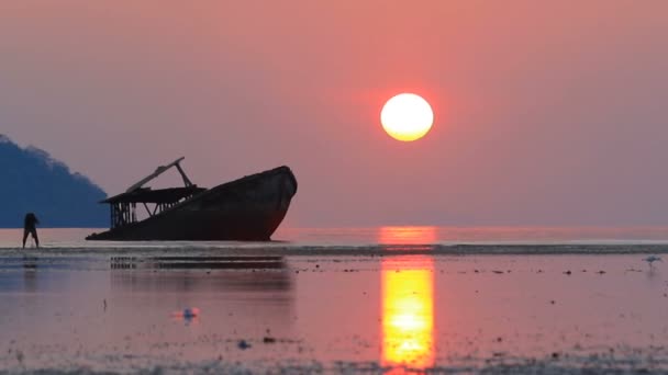 Hombre tomando fotografía de barco arrasado y el sol saliendo del cielo detrás — Vídeo de stock