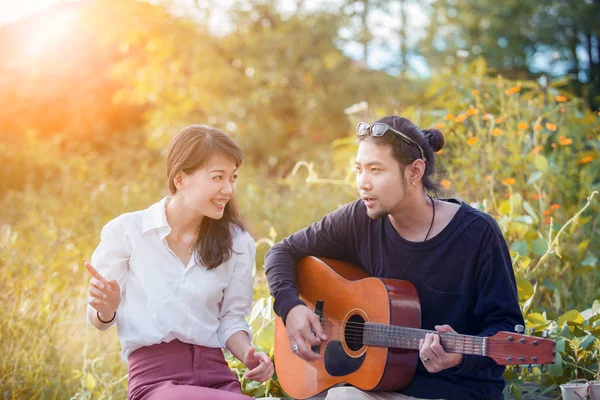 Молодой азиат мужчина и женщина расслабляются играя на гитаре в парке — стоковое фото