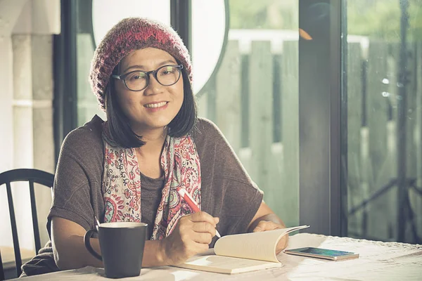 Zahm lächelndes Gesicht einer asiatischen Frau, die im Kaffee ein Taschenbuch liest — Stockfoto