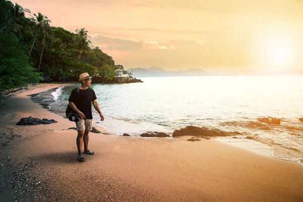 Reisender Mann und DSLR-Kamera laufen am Sandstrand gegen Sonnen — Stockfoto