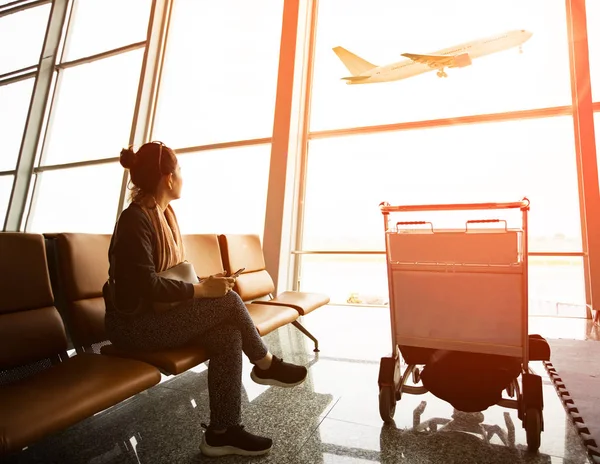 Одинокая женщина, сидящая в аэропорту терминала и пассажирский самолет летать — стоковое фото