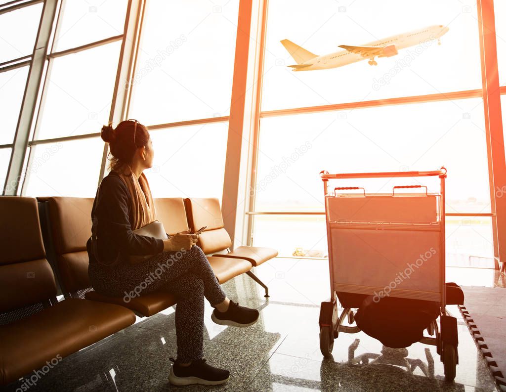 single woman sitting in airport terminal and passanger plane fly