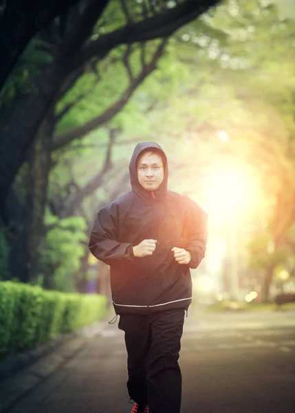 Άθλημα υγιή άνδρα που φοράει σακάκι κουκούλα τρέξιμο σε καταπράσινο πάρκο — Φωτογραφία Αρχείου