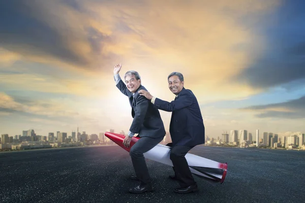 Dois homens de negócios sênior montando em crianças brinquedo de foguete de pé o — Fotografia de Stock