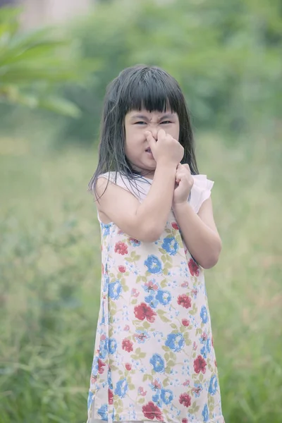 Asian children use hand close her nose standing in green garden — Stock Photo, Image
