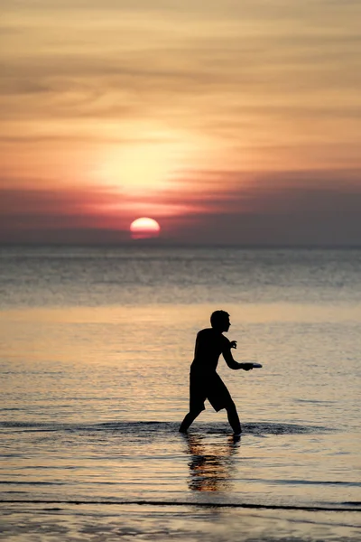 Man spelen vliegende schotel op zee beac tegen mooie avondrood — Stockfoto