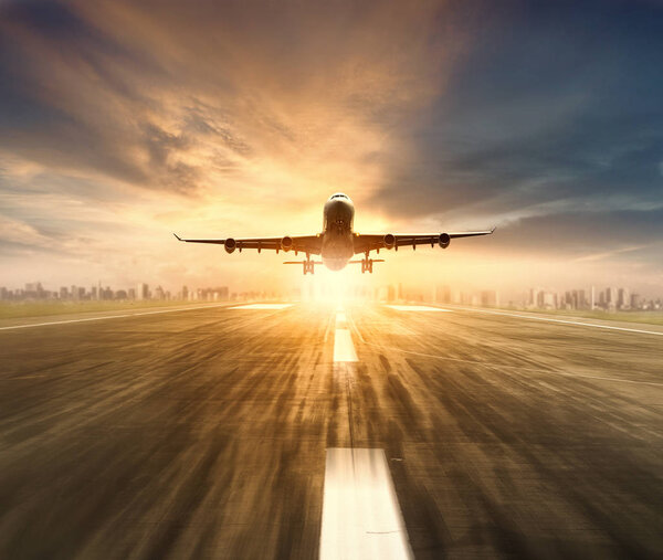 air plane flying over airport runway with city scape and sunset 