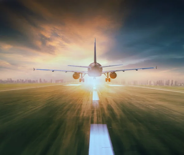Повітряний літак, що літає над злітно-посадковою смугою аеропорту з міським пейзажем і заходом сонця — стокове фото