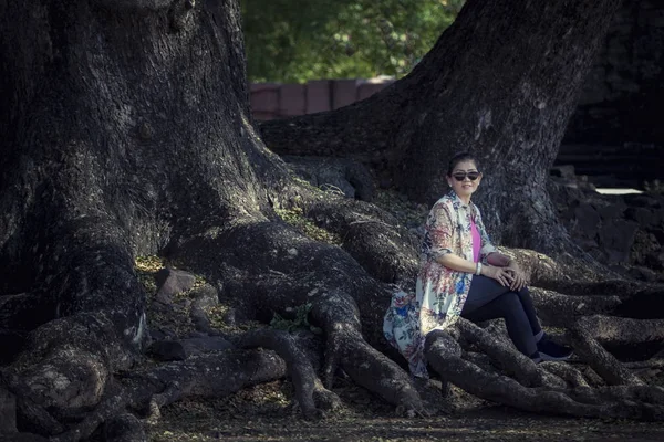 Asiático mujer sentado en Grande lluvia árbol raíz en viajar destinati —  Fotos de Stock