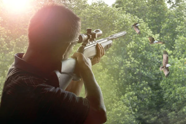 man with long rifle gun approaching for shooting to flying bird