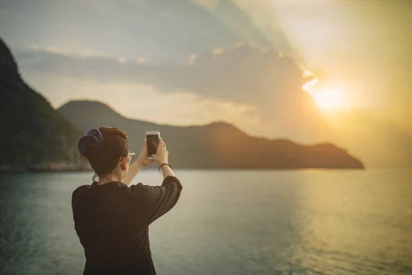 Женщина делает фотографию восхода солнца с помощью смартфона на берегу моря — стоковое фото