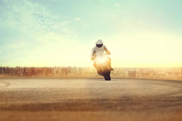 Человек на спортивном мотоцикле по грунтовой дороге против городского здания — стоковое фото