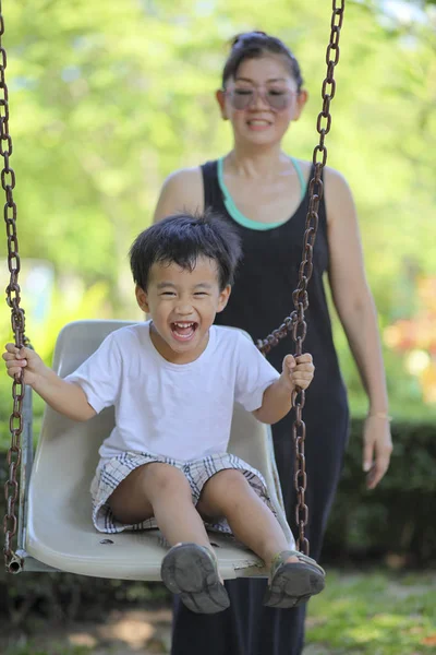 Aziatische kinderen spelen schommel stoel met moeder in groen park — Stockfoto