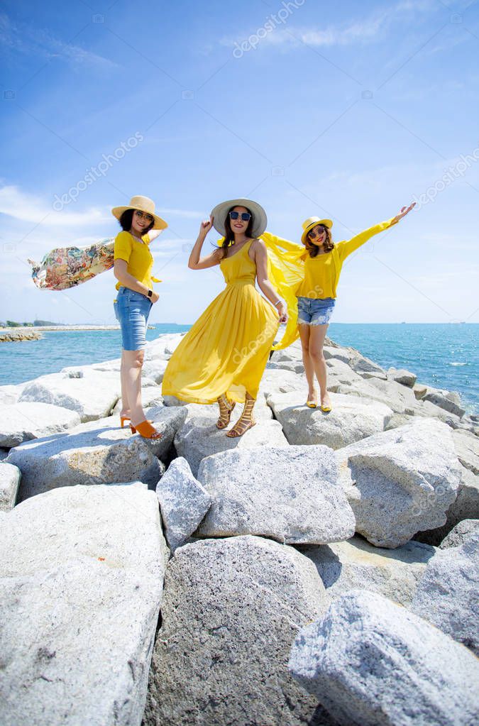 three asian woman wearing yellow clothes standing on sea beach a
