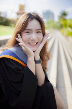 Asyalı genç bir kadının gülümseyen mutlu yüzü üniversite kıyafeti giyiyor.