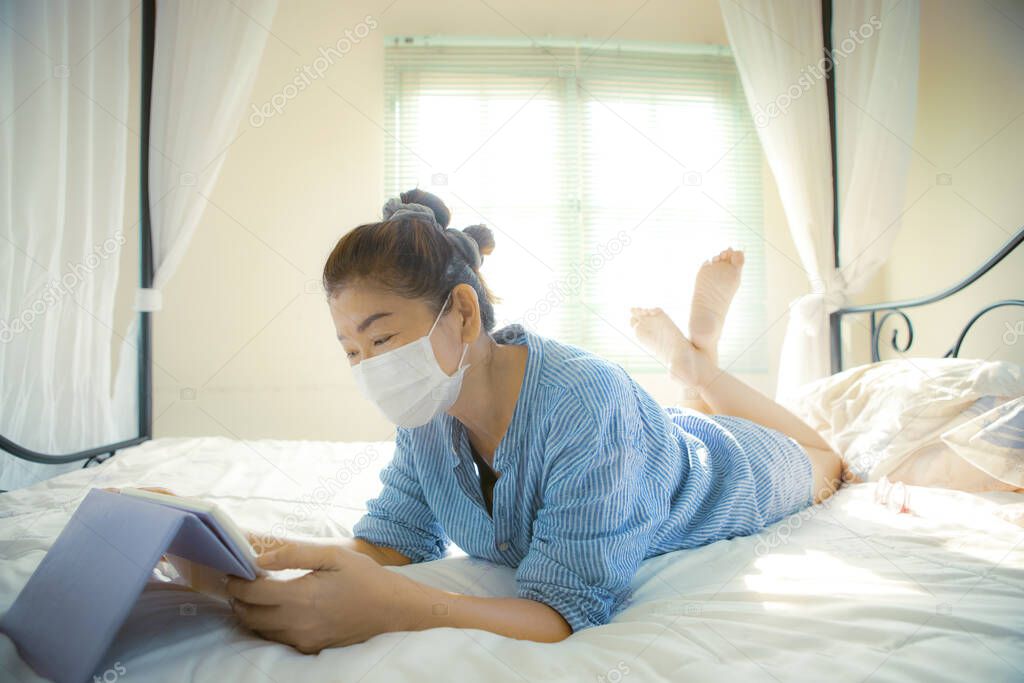 woman quarantine at home wearing protection mask and conect to internet devcie in bedroom