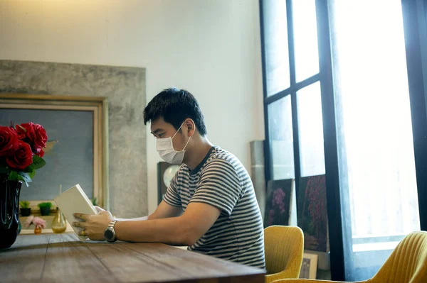 asian man reading book in home living room while quarantine campaign against covid-19 infection