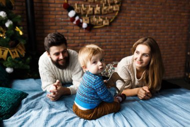 Noel ağacının yanında oğluyla birlikte Noel 'i kutlayan mutlu genç çift. Erkek ve kadın oğluna bakar ve gülümser. Noel ailesi bakışı.