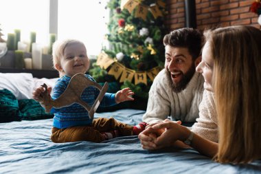 İlk Noel. Çocuk ilk kez Noel Baba 'dan bir hediye alıyor. Neşeli duygular, ebeveynler ve bebek. Yatakta bebek bakıcılığı, Noel ağacı ve arka planda süslemeler.