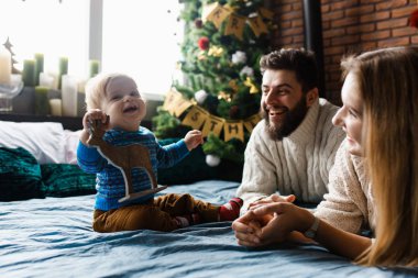 İlk Noel. Çocuk ilk kez Noel Baba 'dan bir hediye alıyor. Neşeli duygular, ebeveynler ve bebek. Yatakta bebek bakıcılığı, Noel ağacı ve arka planda süslemeler.