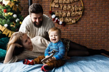 İlk Noel. Mutlu çocuk ilk kez Noel Baba 'dan bir hediye alıyor. Neşeli duygular, ebeveynler ve bebek. Yatakta bebek bakıcılığı, Noel ağacı, arka planda mumlar ve dekorasyonlar.