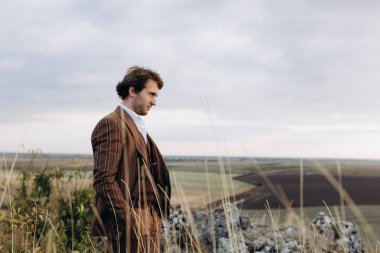 Takım elbiseli genç bir adam tepenin üstünde dikiliyor ve manzaraya bakıyor..