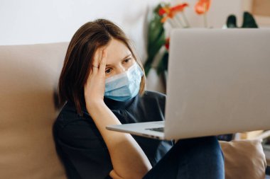 Yüzünde koruyucu maske olan kadın evde kalıyor. Coronavirus 'la ilgili son haberler yüzünden başı ağrıyor. Sosyal uzaklık, karantina, evde kalma. Dünya salgını..
