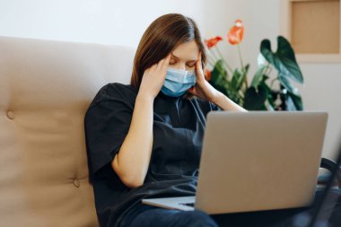 Yüzünde koruyucu maske olan kadın evde kalıyor. Coronavirus 'la ilgili son haberler yüzünden başı ağrıyor. Sosyal uzaklık, karantina, evde kalma. Dünya salgını..