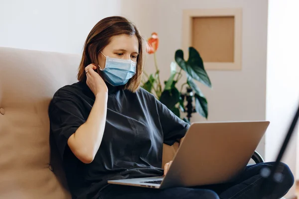 Coronavirus pandemic world. Woman working from home with laptop wearing protective mask. Quarantine, social distancing, stay home concept.
