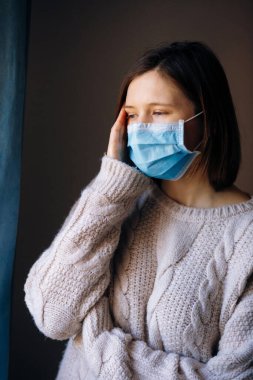 Coronavirus salgınları ve grip salgını sırasında virüs, mikrop ve bakterilerden korunmak için tıbbi maske takan genç bir kadın. Sosyal izolasyon, karantina, evde kalma kavramı.