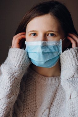 Tıbbi maske takan genç bir kadının yakın plan portresi. Virüs taşıyor, koruyucu maske takıyor. Başkalarına bulaşmasın diye. Sosyal tecrit, karantina, evde kalma. Coronavirüs salgını.