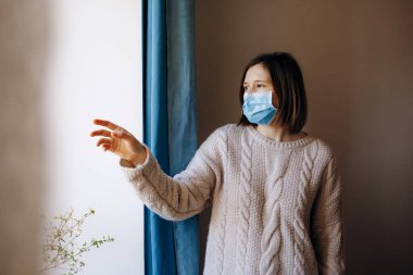 Coronavirus salgınları ve grip salgını sırasında virüslerden, mikroplardan ve bakterilerden korunmak için tıbbi maske takan kadın portresi. Pencereye bakıyorum. Sosyal izolasyon, karantina kavramı.