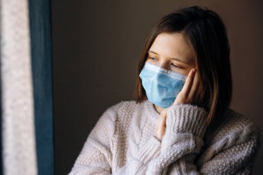 Coronavirus salgınları ve grip salgını sırasında virüs, mikrop ve bakterilerden korunmak için tıbbi maske takan genç bir kadın. Sosyal izolasyon, karantina, evde kalma kavramı.