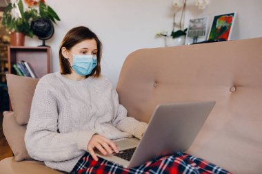 Evde dizüstü bilgisayarlı koruyucu maske takan bir kadın. Karantina, sosyal mesafe, evde kalmak, ofis kavramı. Coronavirüs salgını..