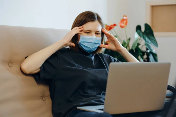 World pandemic. Woman with protective mask on her face isolating at home, reading last news about coronavirus from laptop. Social distancing, stay home concept.