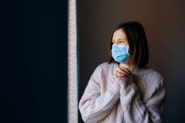 Coronavirus salgınları ve grip salgını sırasında virüslerden, mikroplardan ve bakterilerden korunmak için tıbbi maske takan kadın portresi. Pencereye bakıyorum. Sosyal izolasyon, karantina kavramı.